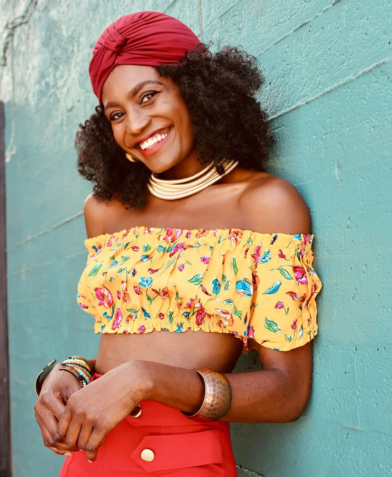 woman in yellow and red floral off shoulder dress leaning on blue wall